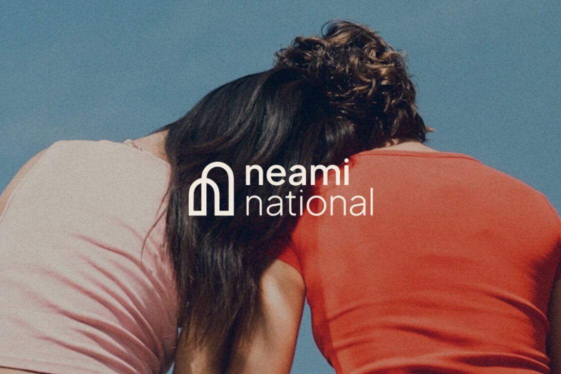 Two people sitting together facing away with one leaning their head on the others soulder. Neami National logo overlaid on top of this image.