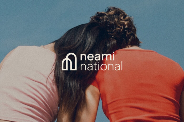 Two people sitting together facing away with one leaning their head on the others soulder. Neami National logo overlaid on top of this image.