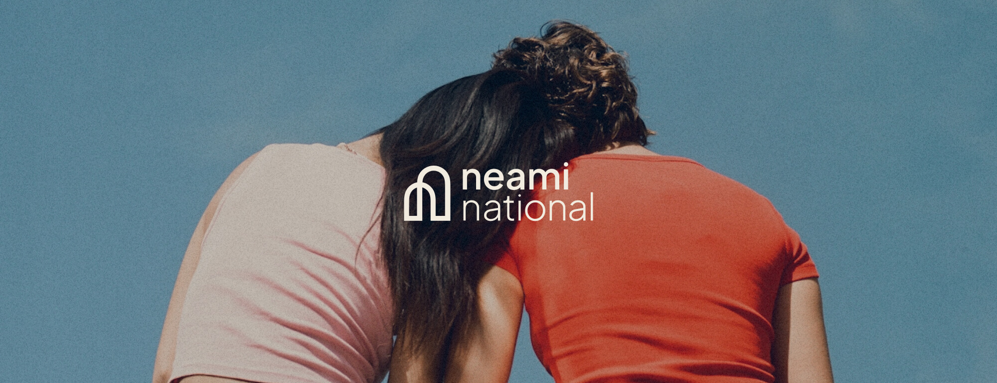 Two people sitting together facing away with one leaning their head on the others soulder. Neami National logo overlaid on top of this image.